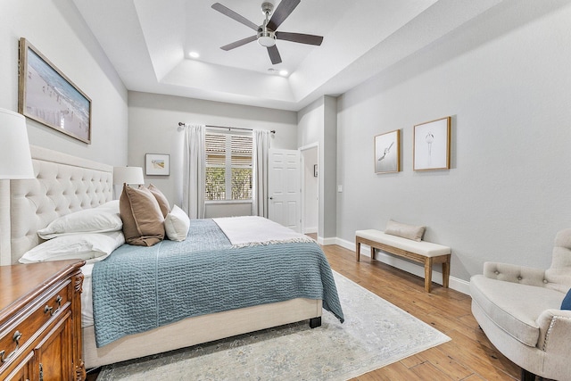 bedroom featuring recessed lighting, a raised ceiling, a ceiling fan, light wood-type flooring, and baseboards