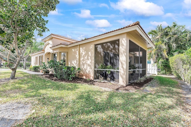 view of side of home featuring a lawn, a sunroom, a tiled roof, fence, and stucco siding