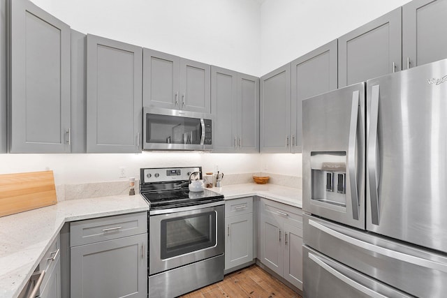 kitchen with stainless steel appliances, light stone counters, gray cabinets, and light wood-style flooring