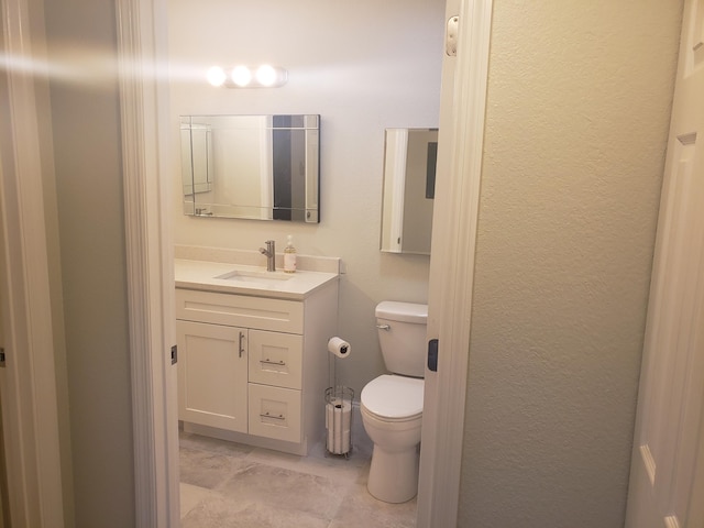 half bathroom with a textured wall, vanity, and toilet