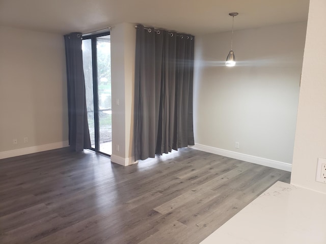 empty room featuring expansive windows, baseboards, and wood finished floors