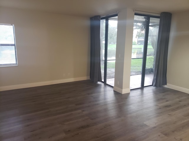 empty room featuring dark wood-style flooring, plenty of natural light, and baseboards