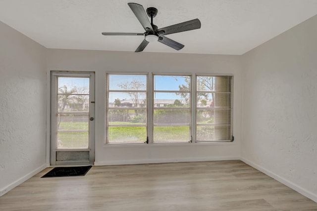 empty room featuring ceiling fan, a textured wall, wood finished floors, and baseboards