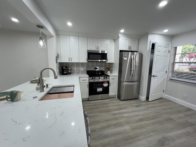 kitchen with light wood-style flooring, a sink, white cabinetry, appliances with stainless steel finishes, and decorative backsplash