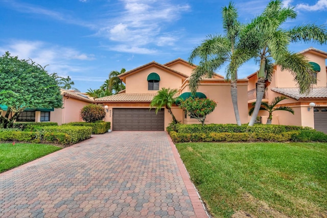 mediterranean / spanish-style house featuring a front yard, a tiled roof, an attached garage, stucco siding, and decorative driveway