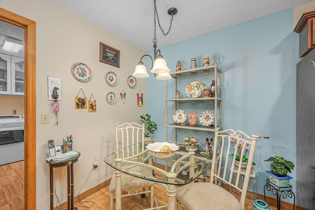 dining room with wood finished floors, baseboards, washer / dryer, a textured ceiling, and a notable chandelier