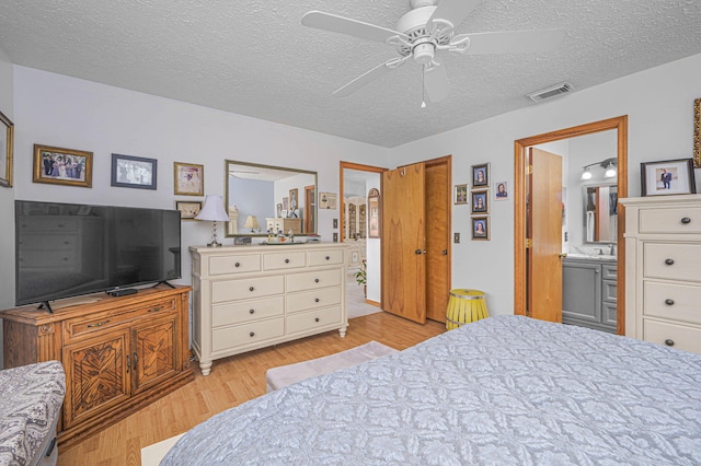 bedroom featuring visible vents, ceiling fan, light wood-type flooring, ensuite bathroom, and a textured ceiling