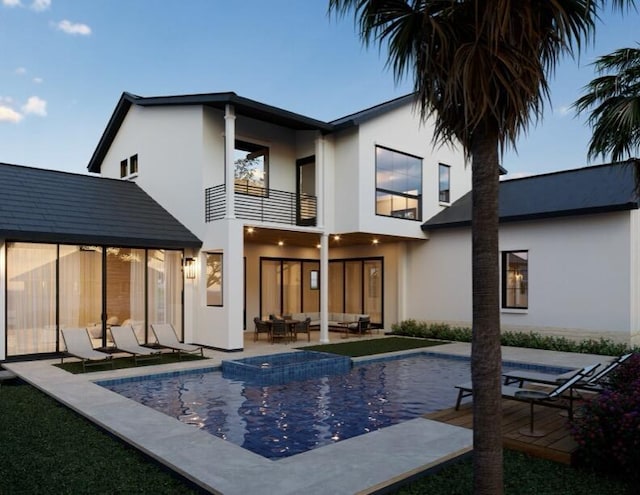 back of property with a balcony, a pool with connected hot tub, an outdoor living space, stucco siding, and a patio area