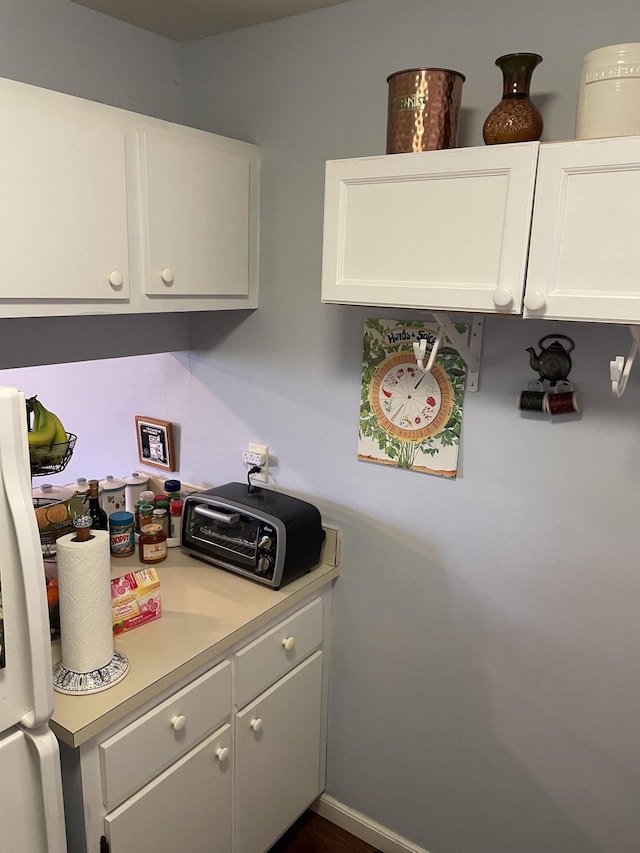 kitchen featuring baseboards, light countertops, a toaster, and white cabinets