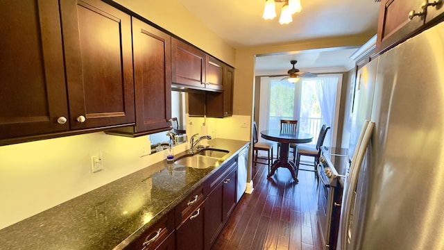 kitchen with appliances with stainless steel finishes, a sink, dark stone countertops, a ceiling fan, and dark wood-type flooring