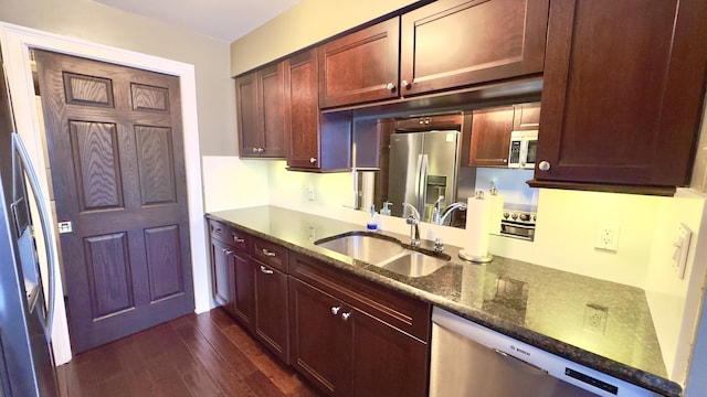 kitchen featuring dark brown cabinets, a sink, dark stone counters, stainless steel appliances, and dark wood-type flooring
