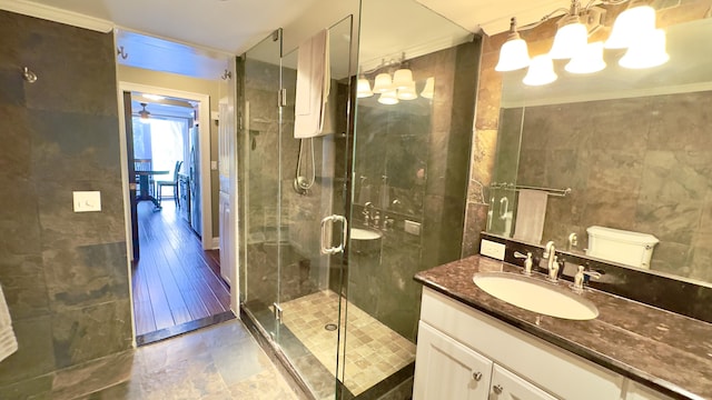 bathroom featuring vanity, ceiling fan with notable chandelier, tile walls, a shower stall, and ornamental molding