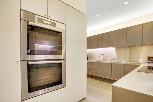 kitchen featuring double oven, black electric cooktop, a sink, light countertops, and modern cabinets