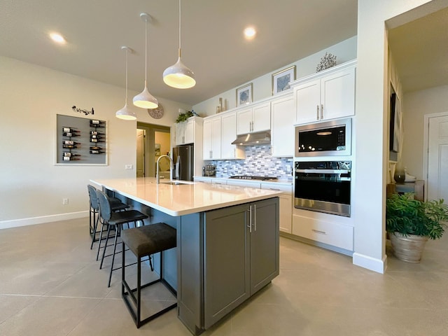 kitchen featuring stainless steel appliances, tasteful backsplash, white cabinets, and under cabinet range hood