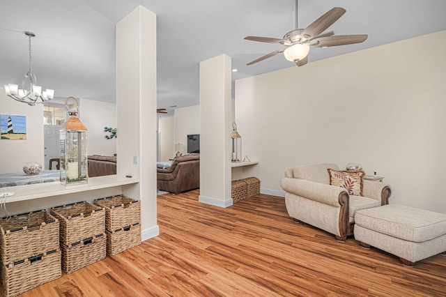 living room with ceiling fan with notable chandelier, wood finished floors, and baseboards