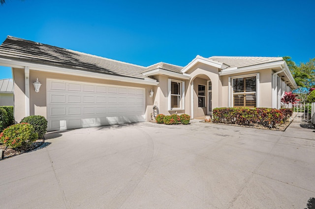 ranch-style house featuring a garage, concrete driveway, a tile roof, and stucco siding