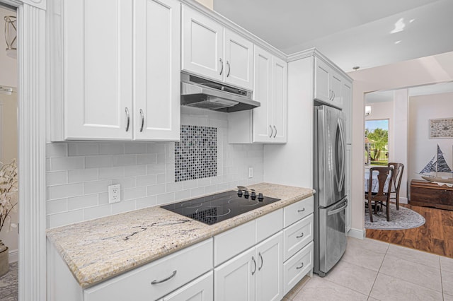 kitchen featuring freestanding refrigerator, white cabinets, under cabinet range hood, and black electric stovetop