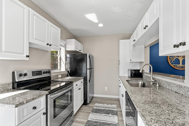 kitchen with baseboards, appliances with stainless steel finishes, light wood-type flooring, white cabinetry, and a sink