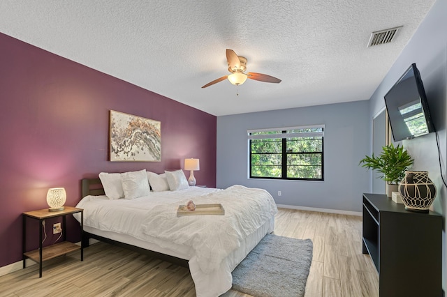 bedroom featuring visible vents, ceiling fan, a textured ceiling, light wood-type flooring, and baseboards