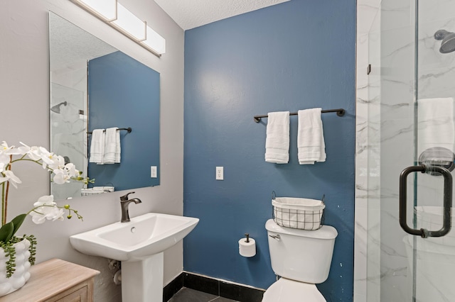 full bathroom featuring a marble finish shower, baseboards, toilet, a textured ceiling, and a sink