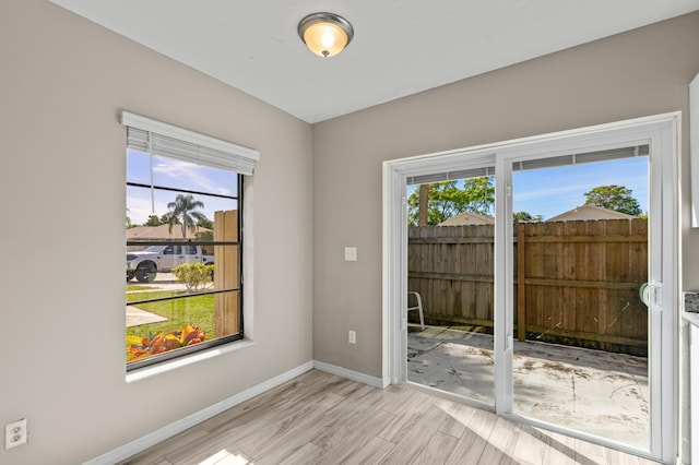 spare room featuring light wood-type flooring, plenty of natural light, and baseboards