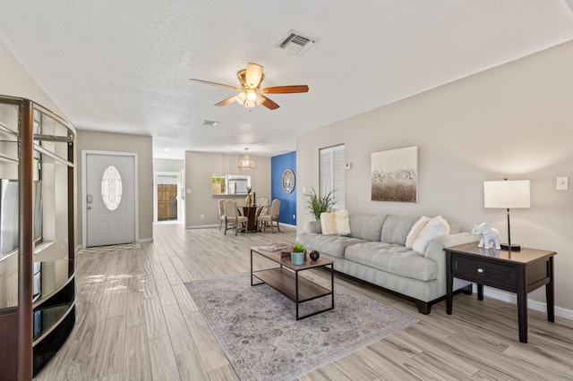 living area featuring visible vents, light wood-style flooring, a ceiling fan, a textured ceiling, and baseboards