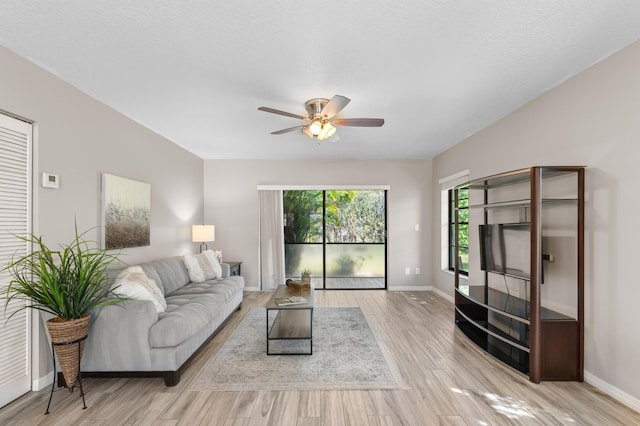 living area featuring light wood-style floors, baseboards, and a ceiling fan