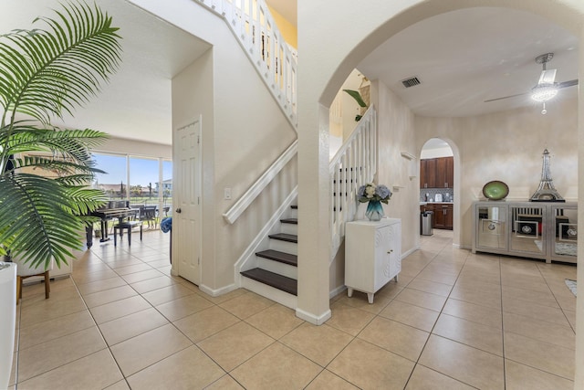 stairs featuring tile patterned floors, visible vents, arched walkways, baseboards, and ceiling fan