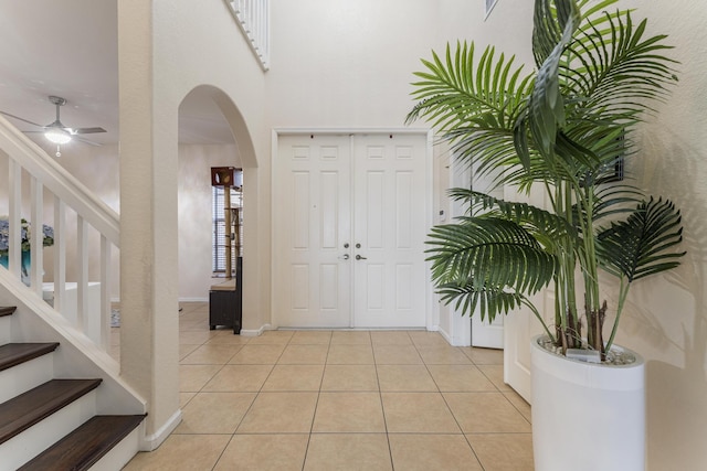 entrance foyer with light tile patterned floors, a ceiling fan, baseboards, arched walkways, and stairs