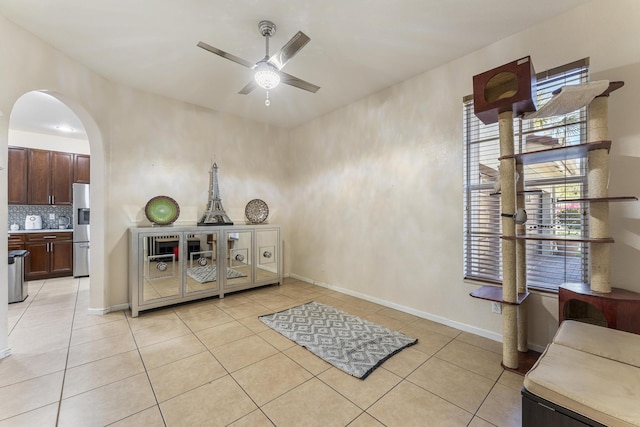 interior space featuring arched walkways, baseboards, a ceiling fan, and light tile patterned flooring