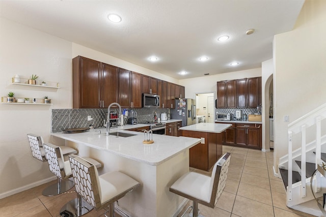 kitchen featuring a breakfast bar area, light countertops, appliances with stainless steel finishes, light tile patterned flooring, and a sink