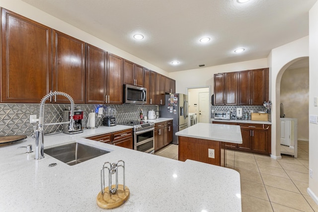 kitchen with light tile patterned floors, arched walkways, a sink, stainless steel appliances, and backsplash