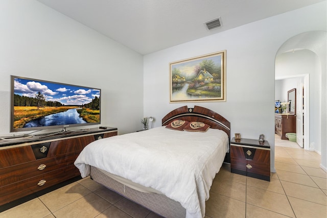 bedroom with light tile patterned floors, visible vents, connected bathroom, and arched walkways