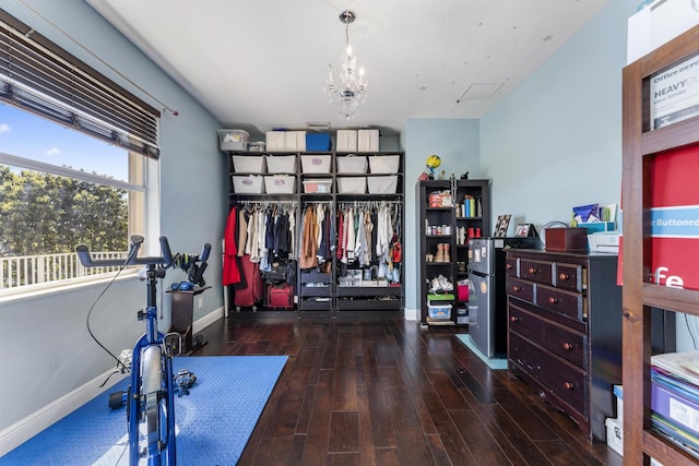 exercise area with a notable chandelier, baseboards, and wood finished floors