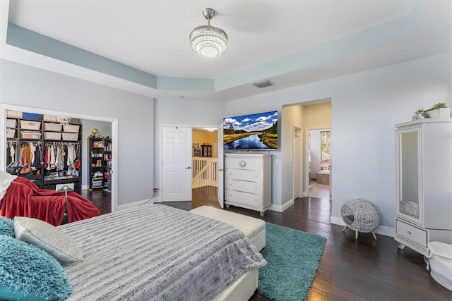 bedroom featuring visible vents, baseboards, a tray ceiling, ensuite bathroom, and wood-type flooring