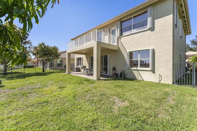 rear view of property featuring stucco siding, a lawn, fence, a balcony, and a patio area