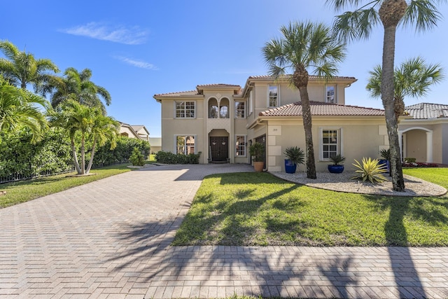 mediterranean / spanish home with a front lawn, a tiled roof, decorative driveway, and stucco siding