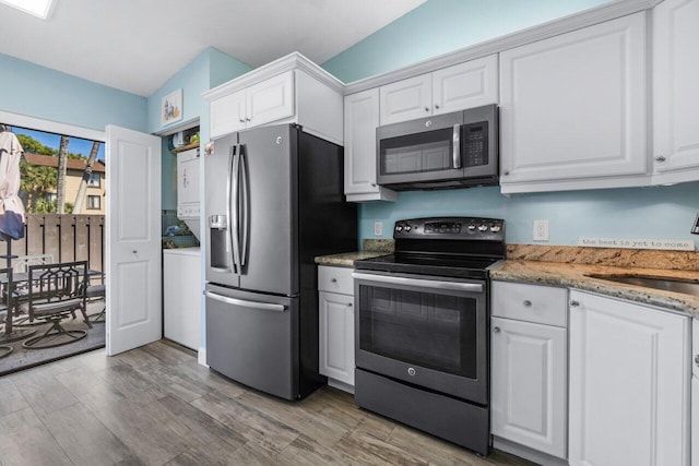 kitchen featuring appliances with stainless steel finishes, stacked washing maching and dryer, a sink, and white cabinets