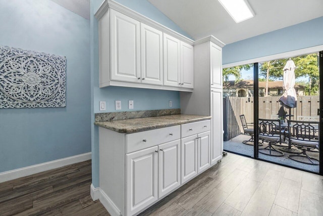 kitchen with lofted ceiling, wood finished floors, baseboards, white cabinets, and light countertops