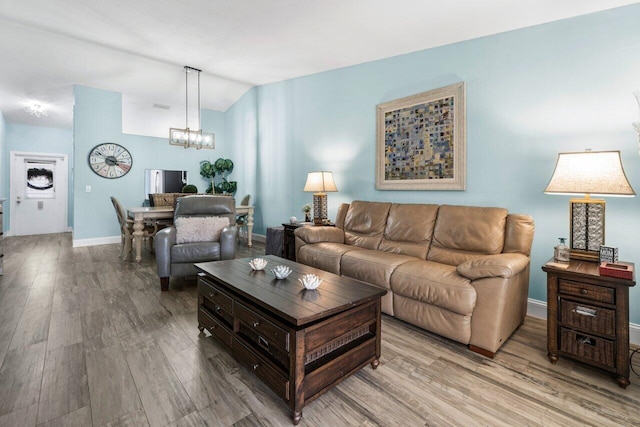 living area with a chandelier, vaulted ceiling, baseboards, and wood finished floors