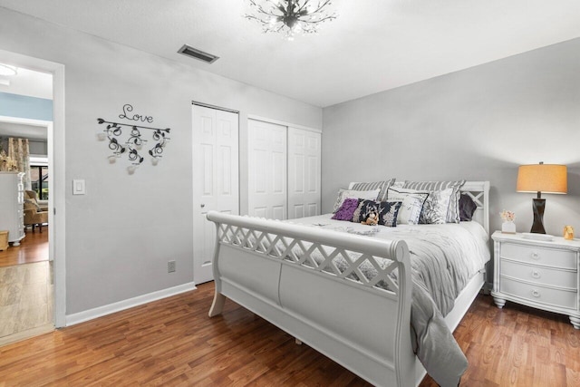 bedroom featuring multiple closets, visible vents, baseboards, and wood finished floors