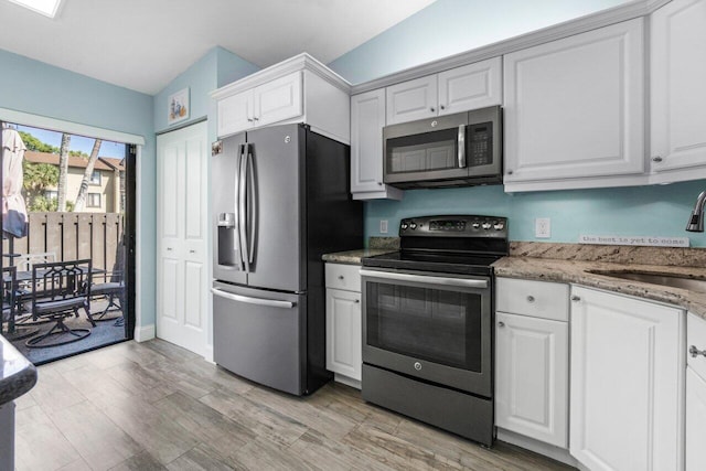 kitchen with white cabinets, light wood-type flooring, stainless steel appliances, and a sink