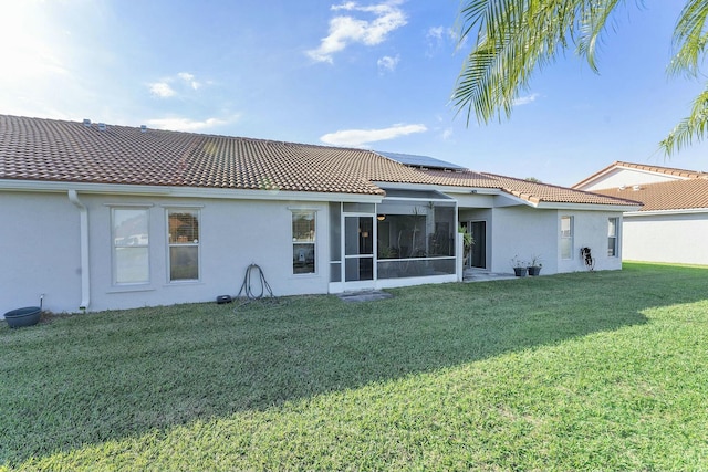 back of property featuring a sunroom, a lawn, roof mounted solar panels, and stucco siding