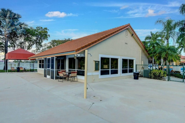 rear view of property with central AC unit, a patio, a sunroom, fence, and stucco siding