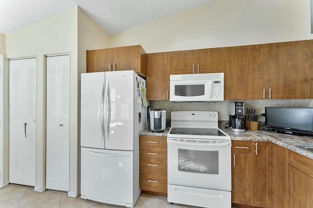 kitchen featuring lofted ceiling, white appliances, light tile patterned floors, and brown cabinets