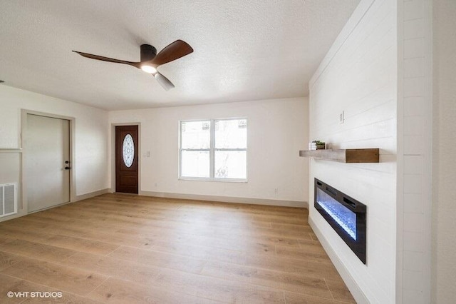 foyer with a large fireplace, ceiling fan, light wood-style flooring, and a textured ceiling