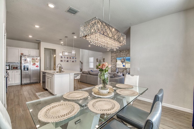 dining space featuring baseboards, visible vents, light wood-style flooring, a textured ceiling, and recessed lighting