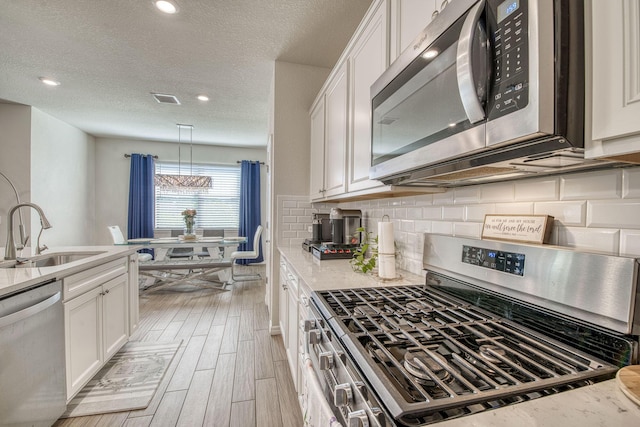 800 SE Villandry Way, Port Saint Lucie, FL 34984 - kitchen featuring stainless steel appliances, a sink, white cabinets, tasteful backsplash, and light wood-style floors