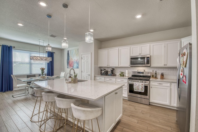 kitchen with a sink, visible vents, appliances with stainless steel finishes, light wood-type flooring, and backsplash