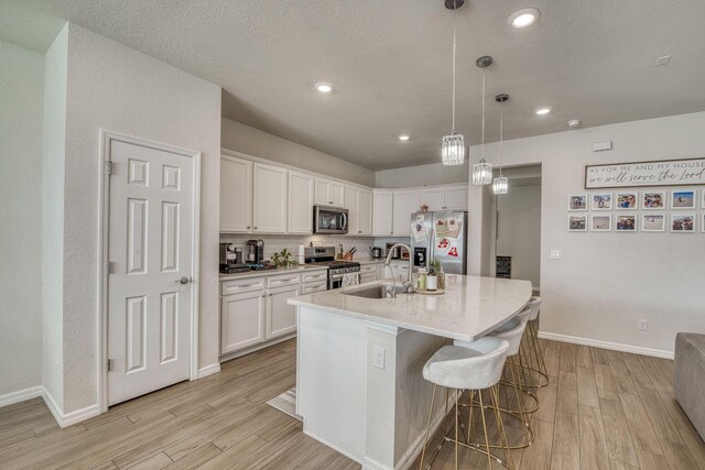 kitchen featuring light wood finished floors, appliances with stainless steel finishes, a kitchen island with sink, white cabinetry, and a sink